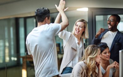 Shot of a group of colleagues giving each other a high five while using a computer together at work